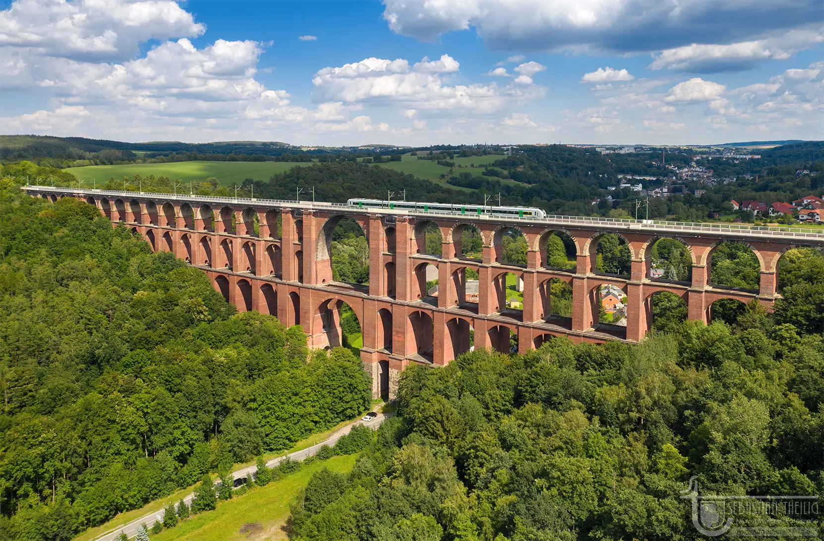 Rote Eisenbahnbrücke mit Zug in grüner Landschaft