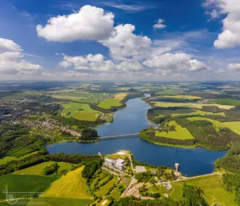 Ein Stausee in grüner Landschaft mit weißen Wolken vor blauem Himmel