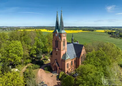 Backsteinkirche mit zwei Türmen in grüner Landschaft