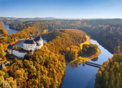 Burg über einem Fluss im Herbstwald