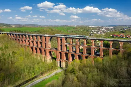 Rote Eisenbahnbrücke mit Zug in grüner Landschaft