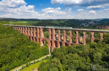 Rote Eisenbahnbrücke mit Zug in grüner Landschaft