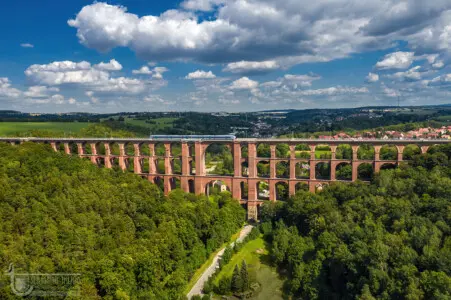Eisenbahnbrücke mit Eisenbahnzug und plastischen Wolken