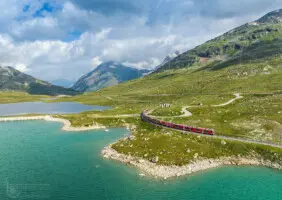 Rote Eisenbahn an grünem See im Hochgebirge