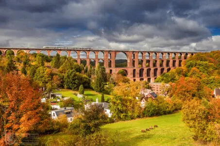 Eisenbahnbrücke im Herbst mit Zug und Schafen vor dunklen Wolken