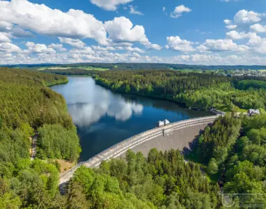 Stausee mit Staumauer und spiegelnden Wolken in grüner Landschaft