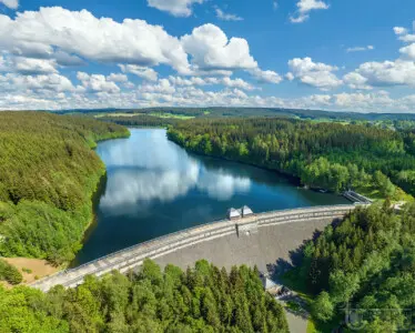Stausee mit Staumauer und spiegelnden Wolken in grüner Landschaft