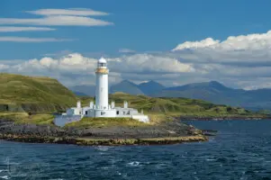 Weißer Leuchtturm auf Felsen am Meer mit Bergen