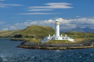 Weißer Leuchtturm auf Felsen am Meer mit Bergen