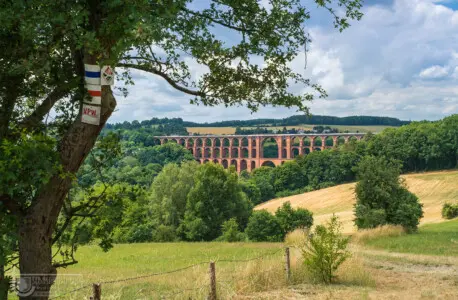 Landschaft mit Wiesen und Bäumen und Eisenbahnbrücke
